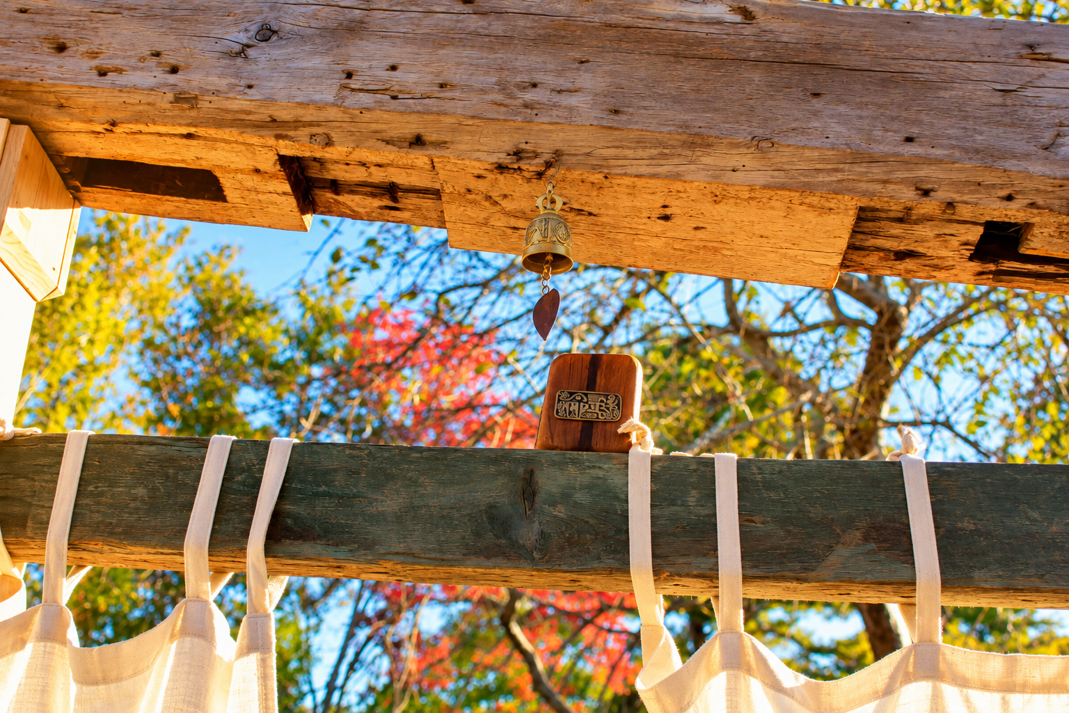 Sunlit wooden structure with a hanging bell and white fabric panels