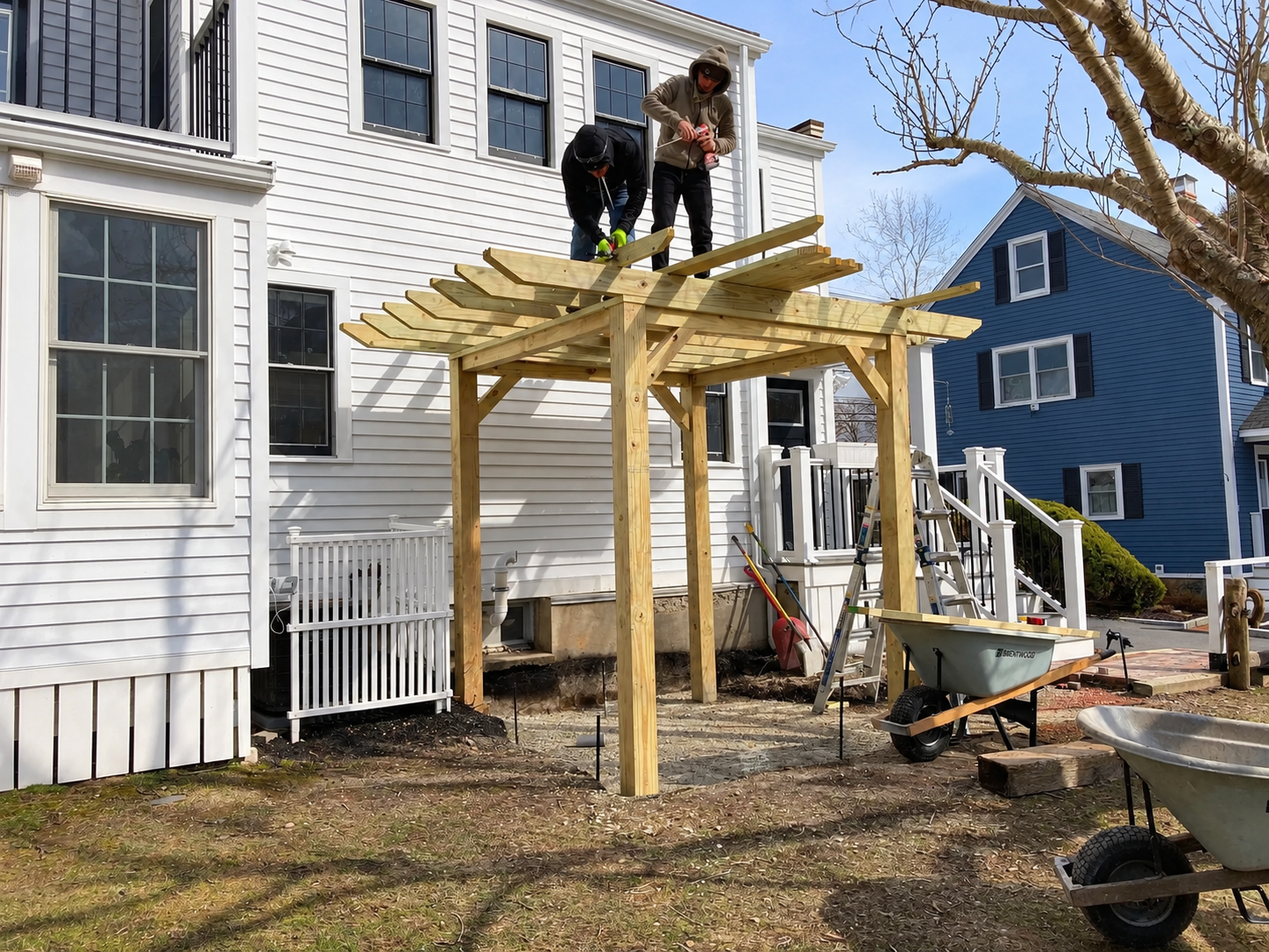 Two landscapers constructing a custom wood pergola beside a home during an outdoor renovation project.