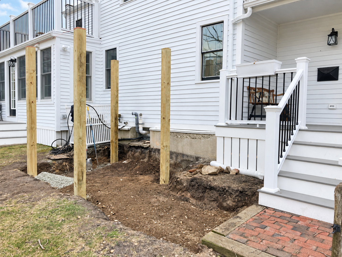 Residential construction project showing newly installed wood posts beside a white home and existing deck.